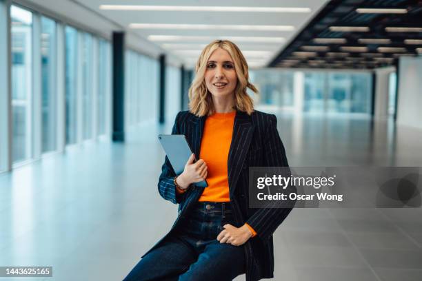 portrait of young businesswoman in blazer with digital tablet, sitting in a modern office space - lgbtq  female fotografías e imágenes de stock