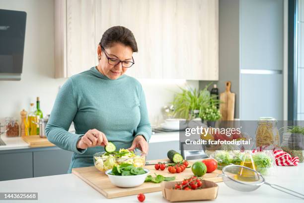 reife frau bereitet gesunden gemüsesalat zu - kitchen worktop stock-fotos und bilder