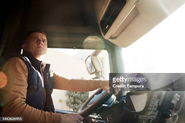 serious truck driver at the steering wheel looking right while turning his semi-truck - chaufför bildbanksfoton och bilder