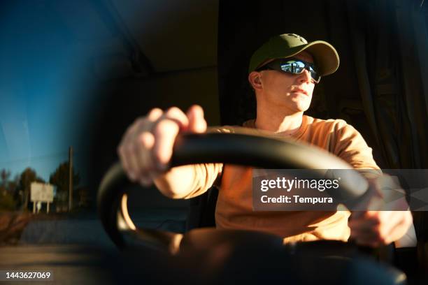 handsome trucker looking through the driver's window while driving - vrachtwagenchauffeur stockfoto's en -beelden