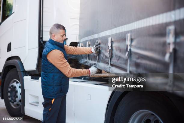 mid adult driver adjusts ratchet tie down straps on truck trailer before departing - trucker stock pictures, royalty-free photos & images