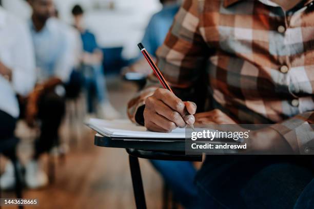 adult writing in the classroom - exam desk stockfoto's en -beelden