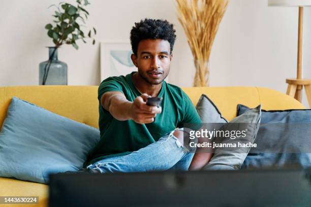entertained man watching a movie on tv turning up the volume, spending a relaxing evening at home. - remote stock pictures, royalty-free photos & images