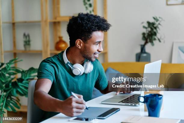 graphic designer working from dining room table at home, using tablet and laptop while doing a design for a client. - diseñador gráfico fotografías e imágenes de stock
