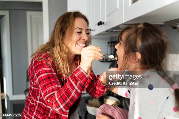 mom cooks in the kitchen and gives her daughter a taste - stew pot stock pictures, royalty-free photos & images