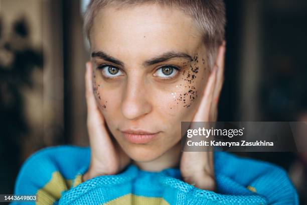 a closeup portrait of a young woman with short hair and glitter on cheeks - short à paillettes photos et images de collection