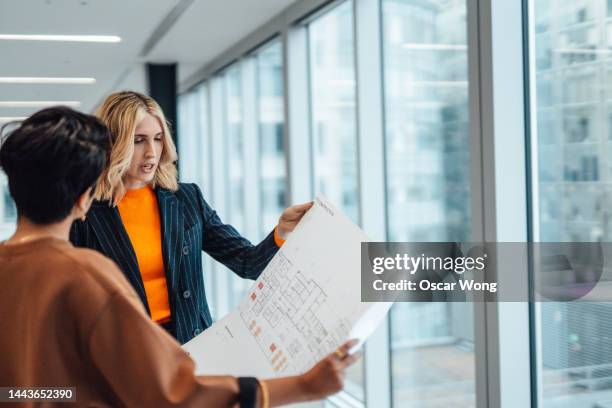 businesswoman having a discussion with her colleague over the floor plan of an empty office space - property developer stock pictures, royalty-free photos & images