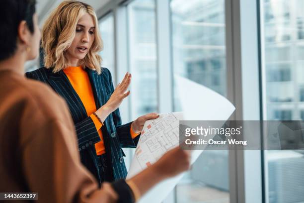 businesswoman having a discussion with her colleague over the floor plan of an empty office space - blueprints stock pictures, royalty-free photos & images