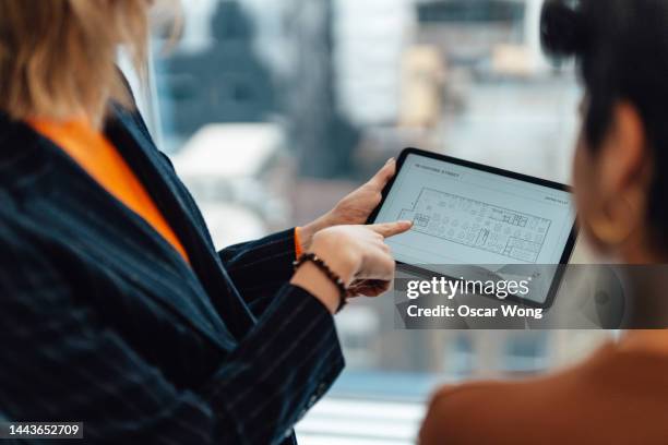 over the shoulder view of businesswoman having a discussion with her colleague over the floor plan of a new office space - plattegrond stockfoto's en -beelden