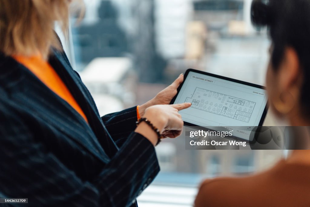 Over the shoulder view of businesswoman having a discussion with her colleague over the floor plan of a new office space