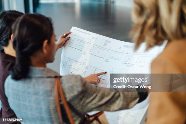 multiracial businesspeople standing in empty office space discussing potential floor plans and layouts of office interior - commercial real estate agent stock pictures, royalty-free photos & images