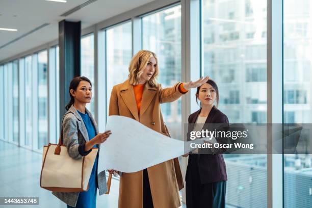 multiracial businesspeople standing in empty office space discussing potential floor plans and layouts of office interior - commercial real estate agent stock pictures, royalty-free photos & images
