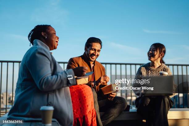 cheerful multi-ethnic business people sitting and having takeaway lunch at rooftop garden at top of office building during lunch break - lunch london stock pictures, royalty-free photos & images