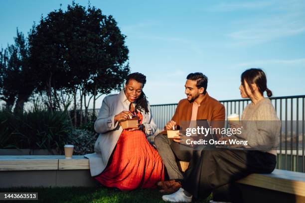 cheerful multi-ethnic business people sitting and having takeaway lunch at rooftop garden at top of office building during lunch break - colleague lunch stock pictures, royalty-free photos & images