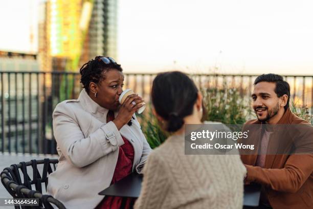 cheerful multi-ethnic business people sitting at rooftop garden at top of office building during coffee break - diverse friends stock pictures, royalty-free photos & images