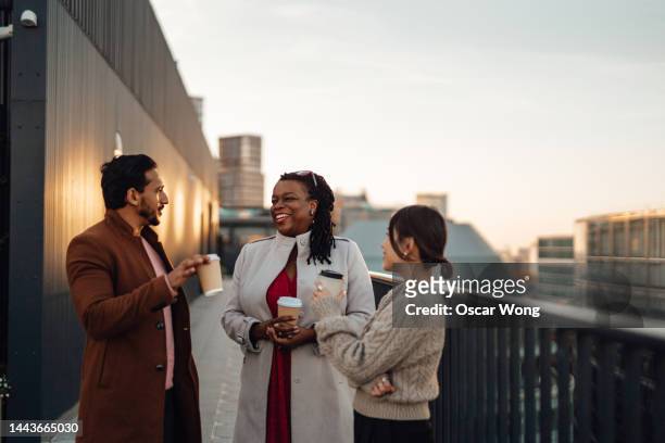 cheerful multi-ethnic business people standing by railing at rooftop during coffee break - enterprise stock pictures, royalty-free photos & images