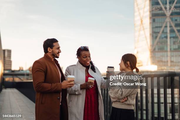 cheerful multi-ethnic business people standing by railing at rooftop during coffee break - wellness stock pictures, royalty-free photos & images