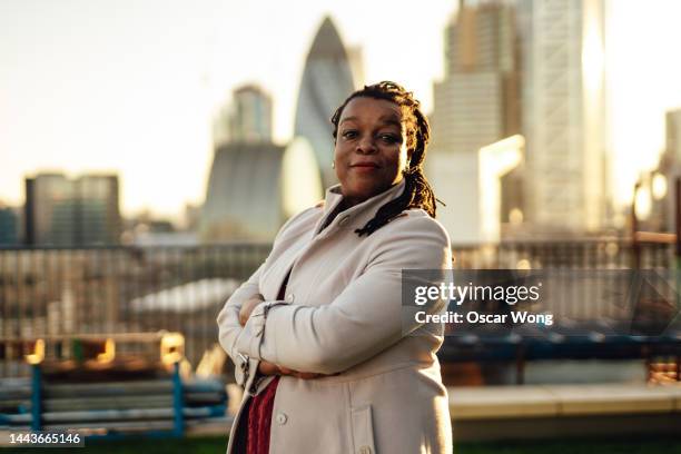 confident businesswoman standing at rooftop garden against london city skyline - waist up stock pictures, royalty-free photos & images