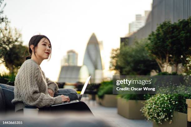 young asian businesswoman working on laptop in rooftop garden against london cityscape - insurance stock pictures, royalty-free photos & images