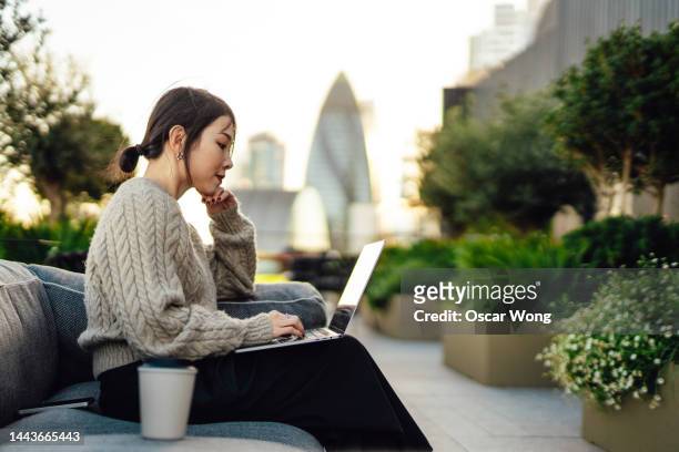 young asian businesswoman working on laptop in rooftop garden against london cityscape - digital business london stockfoto's en -beelden