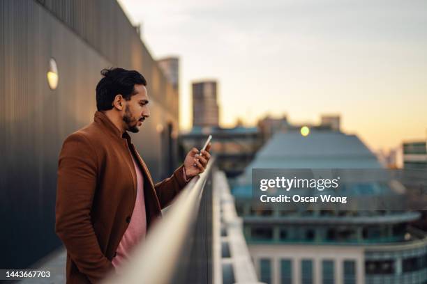 businessman working and talking on phone on rooftop against london cityscape - conversation sunset stock-fotos und bilder