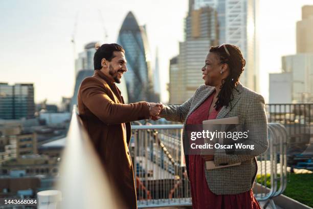 businesspeople making handshake on rooftop against london cityscape - deal england stock-fotos und bilder