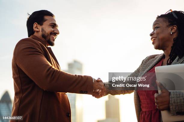 businesspeople making handshake on rooftop against london cityscape - chance encounter stock pictures, royalty-free photos & images