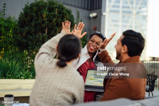coworkers giving each other a high five in a meeting at rooftop garden in high-rise office building - environmental conservation business stock pictures, royalty-free photos & images