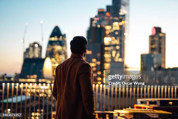 businessman looking over city at rooftop in high-rise business building - city of london stock pictures, royalty-free photos & images