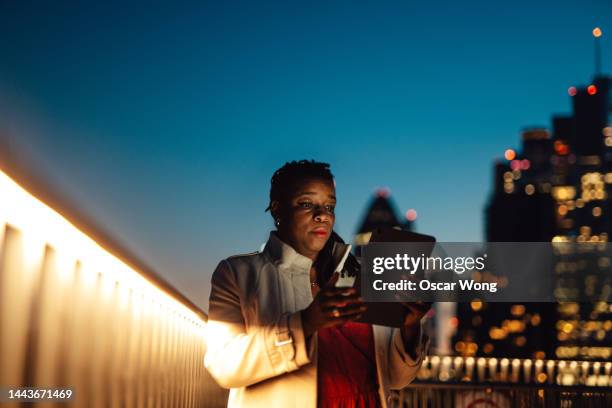 businesswoman using digital tablet at rooftop in business building against illuminated financial buildings and london cityscape at night - urban life stock pictures, royalty-free photos & images