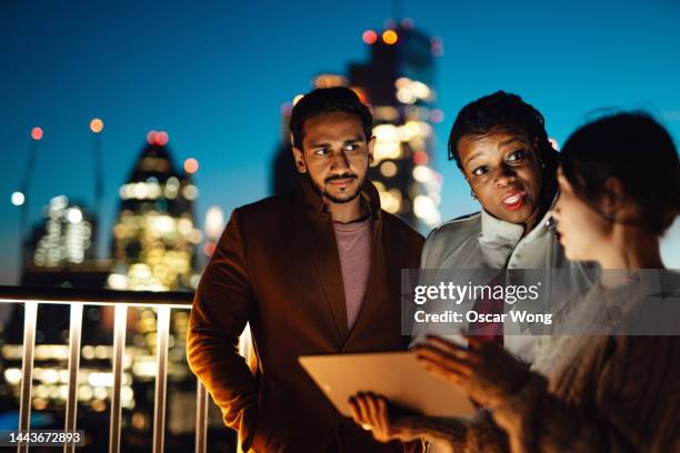 coworkers working and talking at rooftop against london cityscape at night - chinese businessman stock pictures, royalty-free photos & images