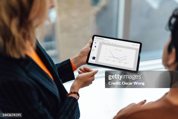 female financial advisor giving business advise to her client with graphs and data shown on digital tablet - 2 people back asian imagens e fotografias de stock