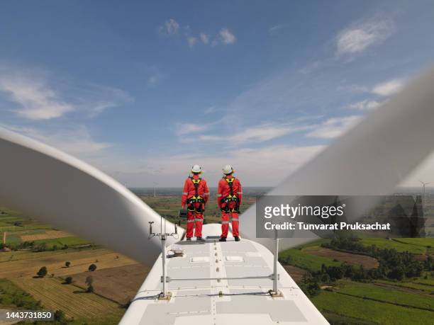 two electric engineer wearing full personal protective equipment working on top of wind turbine farm. - wind mill stockfoto's en -beelden