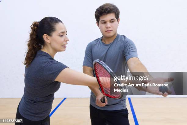 der trainer weist seinen lehrling an, wie er den schläger und den ball zum aufschlag aufnimmt. - squash racquet stock-fotos und bilder