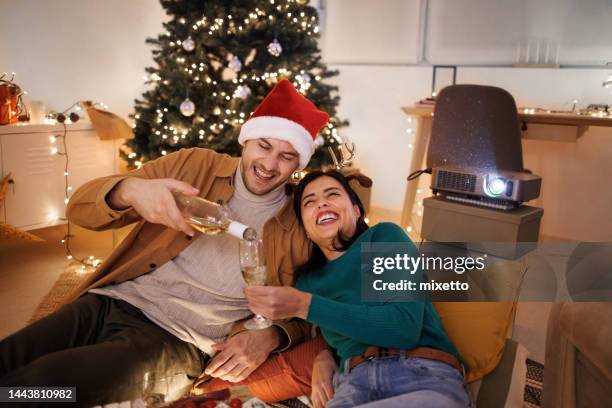 young smiling couple enjoying wine while having  romantic movie night in their apartment - young couple date night wine stock pictures, royalty-free photos & images