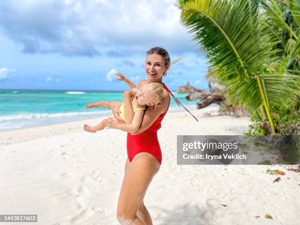 happy adorable baby girl  with her beautiful mother laughing while playing  in the sand during summer holidays on a sea beach. - happy holidays family stock pictures, royalty-free photos & images
