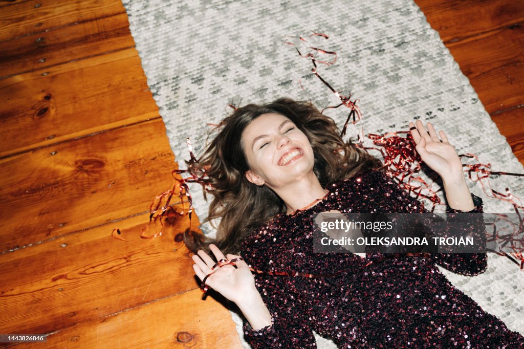 Happy young woman in glittering cocktail dress on carpet floor, flash light, user generated content