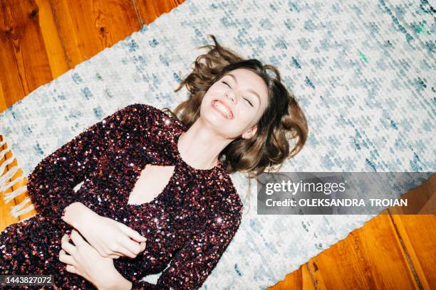 happy young woman in glittering cocktail  dress on carpet floor, flash light, user generated content - ropa tirada en el suelo fotografías e imágenes de stock