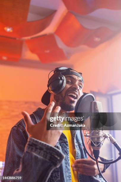 black male music artist with headphones singing into the microphone - rap stockfoto's en -beelden