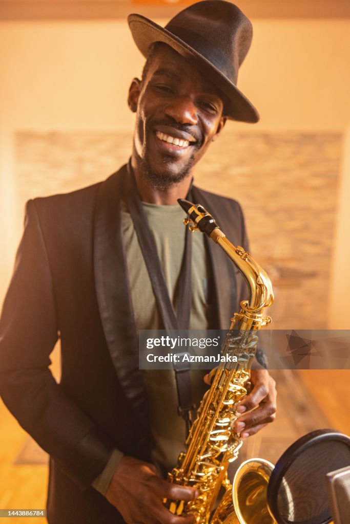 Adult Black Musician With A Hat Holding A Saxophone And Smiling At The Camera