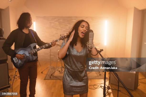 young adult black female singer holding headphones and recording a song in a beautiful studio - rhythm and blues stockfoto's en -beelden