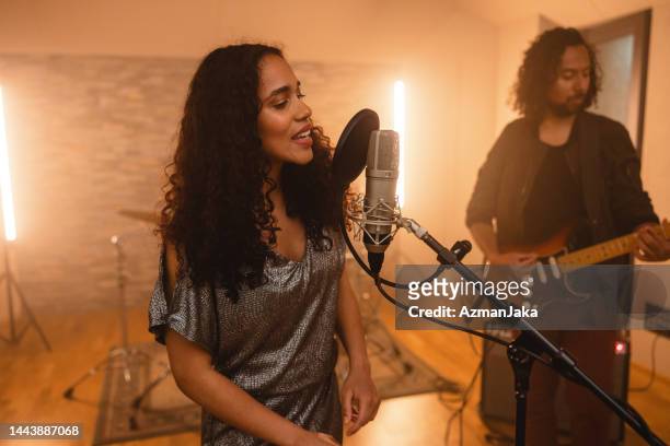 young adult black female lead singer recording a song in a music studio with a black male guitarist - lead singer stock pictures, royalty-free photos & images