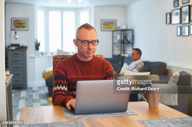 mature man using a laptop in his living room - chap stock pictures, royalty-free photos & images