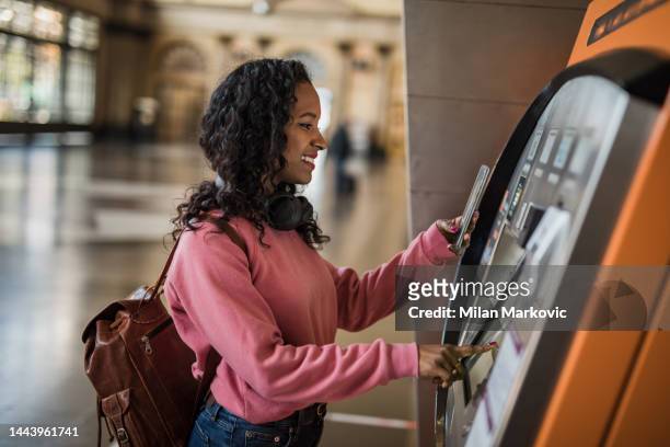a beautiful young woman uses an atm at a metro station in barcelona, withdraws her money to go shopping - bank account stock pictures, royalty-free photos & images