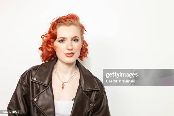 studio portrait of a young red-haired white woman in a black leather jacket on a white background - dyed hair stock pictures, royalty-free photos & images