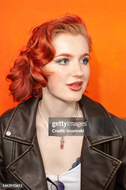 close-up studio portrait of a young red-haired white woman in a black leather jacket on an orange background - bobbed hair stock pictures, royalty-free photos & images