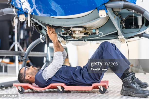 african american aviation engineer lying on roller creeper and repairing helicopter - jet lag stockfoto's en -beelden