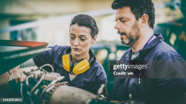 experienced aviation mechanic teaching colleague repairing helicopter part, close up on faces - vliegtuigmonteur stockfoto's en -beelden