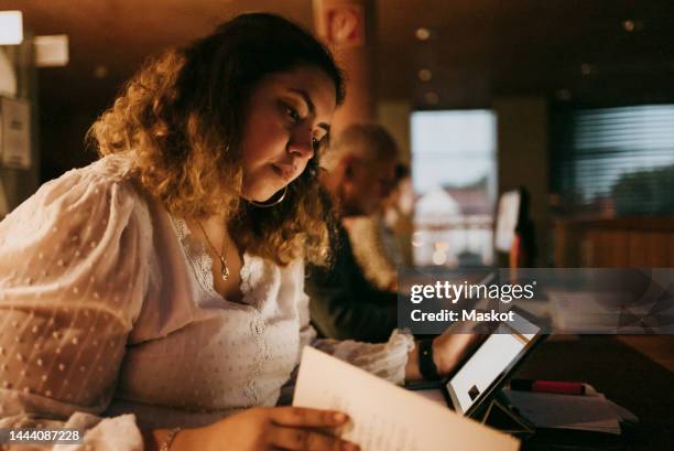 young student reading book while studying in illuminated library at college - perfeccionamiento profesional fotografías e imágenes de stock
