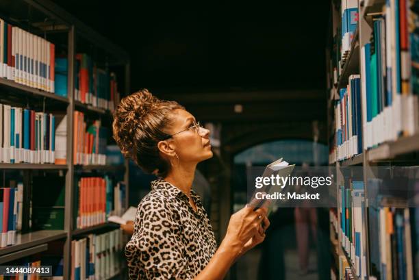 female university student choosing book from shelf in library - library　woman stockfoto's en -beelden